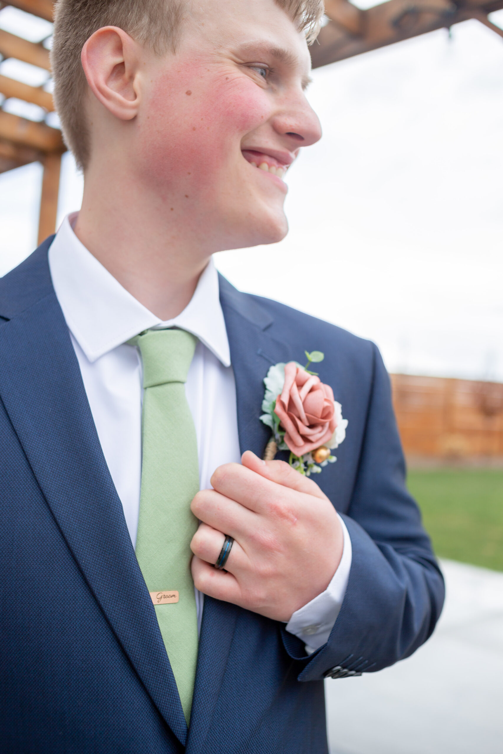 groom smiling and looking off in the distance while holding a 'groom' tie clip